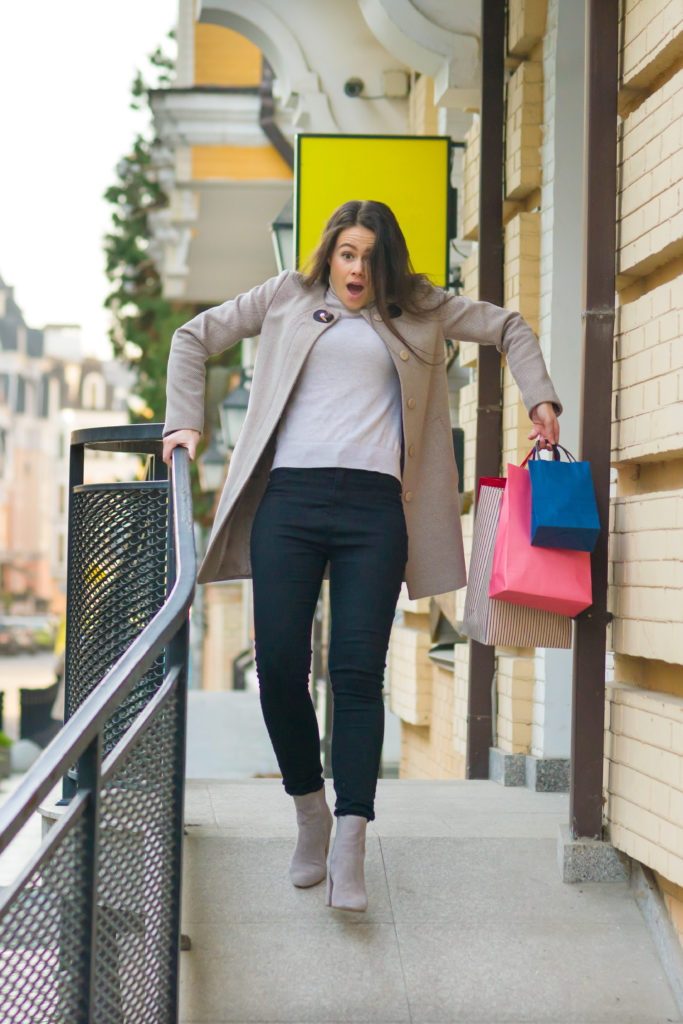 Young woman coming out of a store with shopping bags slipping on a sidewalk